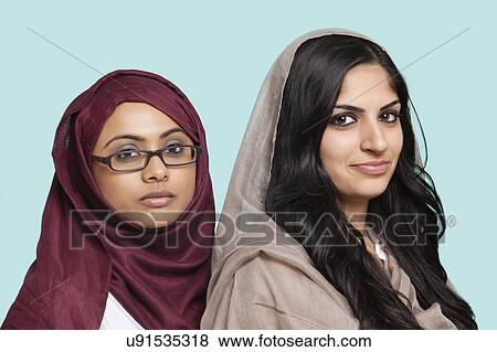 Stock Photo - Portrait of two young Muslim women in traditional clothing against blue background. Fotosearch