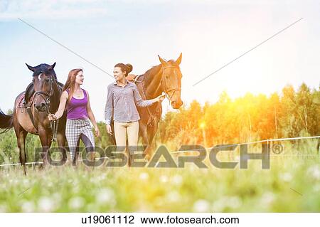 Stock Image - Portrait of women walking while talking with their horses in ranch. Fotosearch