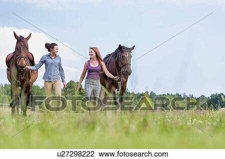 Stock Image - Portrait of women walking while talking with their horses in ranch. Fotosearch