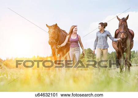 Stock Image - Portrait of women walking while talking with their horses in ranch. Fotosearch