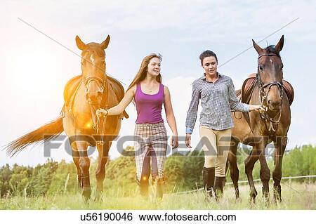 Stock Photograph - Portrait of women walking while talking with their horses in ranch. Fotosearch