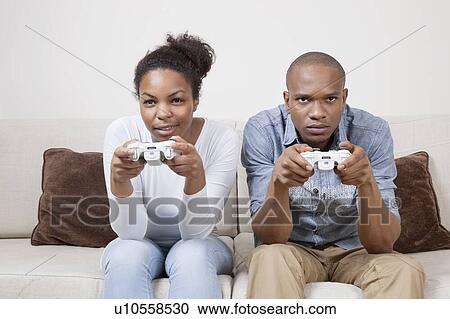 Stock Image - Portrait of young African American couple playing video game. Fotosearch