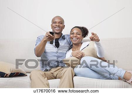 Stock Photograph - Portrait of young African American couple watching TV at home. Fotosearch