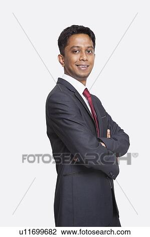Stock Image - Portrait of young Asian businessman in suit with arms crossed against white background. Fotosearch