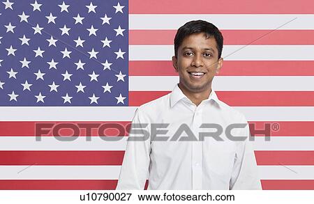 Stock Photo - Portrait of young Asian man in shirt smiling against American flag. Fotosearch
