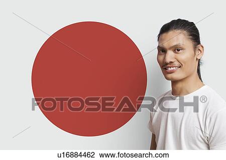 Stock Image - Portrait of young Asian man smiling against Japanese flag. Fotosearch