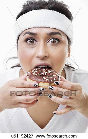 Stock Photo - Portrait of young Asian woman eating donut over white background. Fotosearch