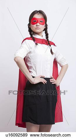 Stock Photo - Portrait of young Asian woman in superhero costume with hands on hips against white background. Fotosearch