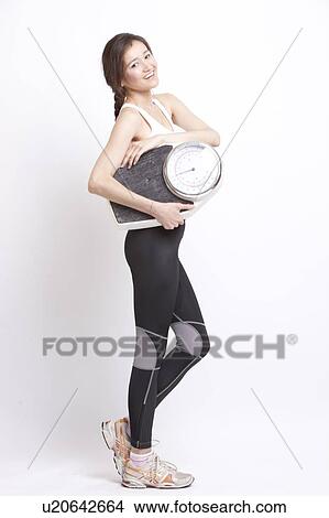 Picture - Portrait of young Asian woman with weight scale against white background. Fotosearch