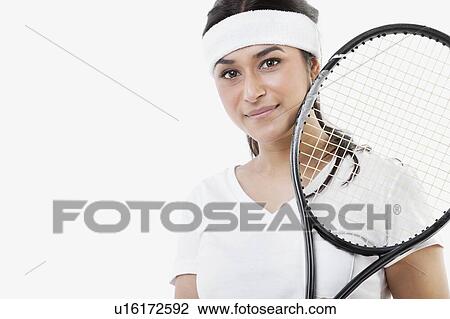 Stock Image - Portrait of young Asian woman with tennis racket against white background. Fotosearch