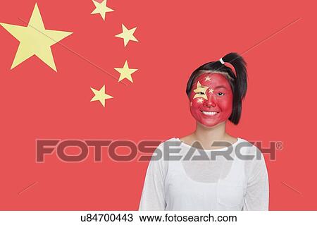 Stock Image - Portrait of young Asian woman with painted face smiling against Chinese flag. Fotosearch