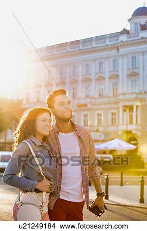 Portrait of young attractive couple walking in the middle of the city with lens flare in background View Large Photo Image Picture - Portrait of young attractive couple walking in the middle of the city with lens flare in background. Fotosearch