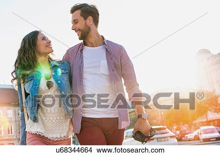 Portrait of young attractive couple walking in the middle of the city with lens flare in background View Large Photo Image Picture - Portrait of young attractive couple walking in the middle of the city with lens flare in background. Fotosearch