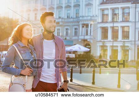 Portrait of young attractive couple walking in the middle of the city with lens flare in background View Large Photo Image Stock Image - Portrait of young attractive couple walking in the middle of the city with lens flare in background. Fotosearch