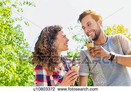 Stock Image - Portrait of young attractive couple walking while eating ice cream. Fotosearch
