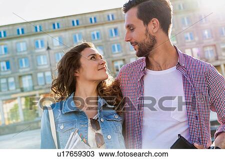 Stock Image - Portrait of young attractive couple standing against museum with lens flare in background. Fotosearch