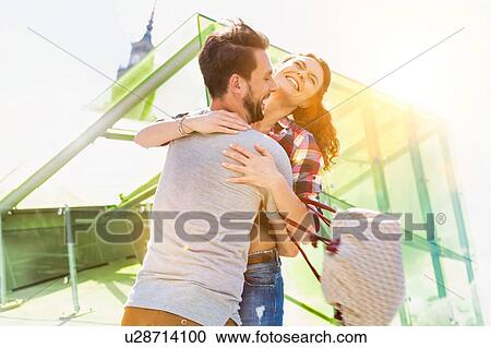 Stock Image - Portrait of young attractive couple standing while hugging each other in the middle of the city with lens flare in bakcground. Fotosearch