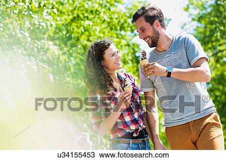 Stock Image - Portrait of young attractive couple walking while eating ice cream. Fotosearch
