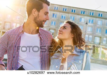 Stock Photo - Portrait of young attractive couple standing against museum with lens flare in background. Fotosearch