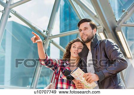 Stock Photo - Portrait of young attractive couple looking on the map in the middle of the city. Fotosearch