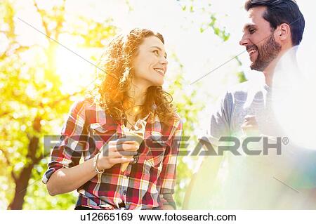 Stock Photo - Portrait of young attractive couple walking while eating ice cream with lens flare in background. Fotosearch