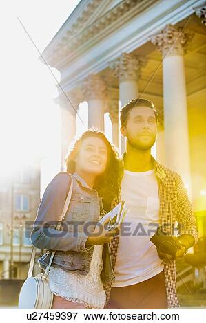Stock Photo - Portrait of young attractive couple standing against museum with lens flare in background. Fotosearch