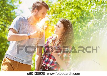 Stock Photo - Portrait of young attractive couple walking while eating ice cream with lens flare in background. Fotosearch