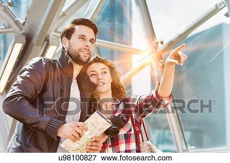 Stock Photo - Portrait of young attractive couple looking on the map in the middle of the city with lens flare in background. Fotosearch