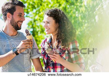 Portrait of young attractive couple walking while eating ice cream with lens flare in background View Large Photo Image Stock Photograph - Portrait of young attractive couple walking while eating ice cream with lens flare in background. Fotosearch