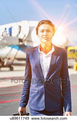 Stock Photo - Portrait of young attractive flight attendant standing against airplane in airport. Fotosearch