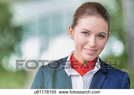 Stock Photography - Portrait of young attractive flight attendant standing against flight display monitor in airport. Fotosearch