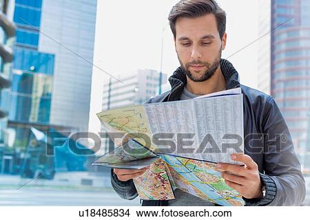 Picture - Portrait of young attractive man looking on the map in the city. Fotosearch