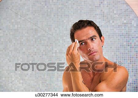 Portrait of young attractive man cleansing his face with cotton and toner in the bathroom View Large Photo Image Picture - Portrait of young attractive man cleansing his face with cotton and toner in the bathroom. Fotosearch