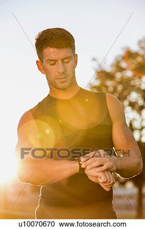 Portrait of young attractive man looking at his wristwatch in park with lens flare View Large Photo Image Stock Image - Portrait of young attractive man looking at his wristwatch in park with lens flare. Fotosearch