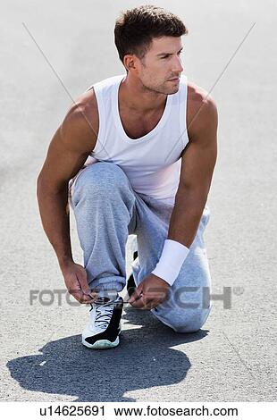 Portrait of young attractive man wearing sports wear tying his rubber shoes in park View Large Photo Image Stock Image - Portrait of young attractive man wearing sports wear tying his rubber shoes in park. Fotosearch