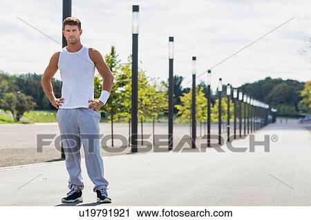 Stock Image - Portrait of young attractive man wearing sports wear standing in park. Fotosearch