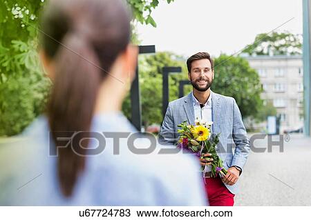 Stock Image - Portrait of young attractive man holding boquet of flowers for his girlfriend in park. Fotosearch