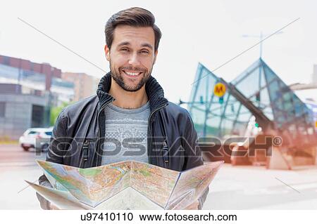 Stock Image - Portrait of young attractive man looking on the map in the city. Fotosearch