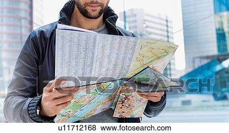 Stock Photo - Portrait of young attractive man looking on the map in the city with lens flare in background. Fotosearch