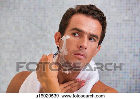 Portrait of young attractive man shaving his beard while looking in the mirror View Large Photo Image Stock Photo - Portrait of young attractive man shaving his beard while looking in the mirror. Fotosearch