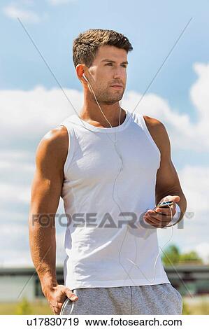 Portrait of young attractive man standing while using and listening to music on his smartphone in park View Large Photo Image Stock Photo - Portrait of young attractive man standing while using and listening to music on his smartphone in park. Fotosearch