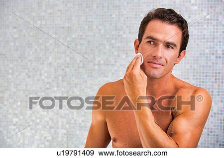 Stock Photo - Portrait of young attractive man cleansing his face with cotton and toner in the bathroom. Fotosearch