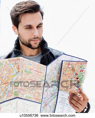 Stock Photograph - Portrait of young attractive man looking on the map in the city with lens flare in background. Fotosearch