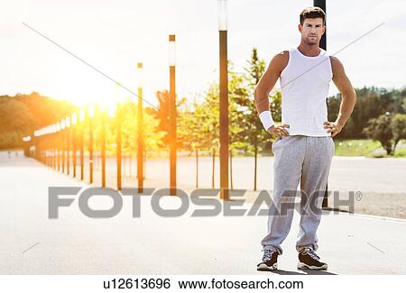 Stock Photograph - Portrait of young attractive man wearing sports wear standing in park. Fotosearch