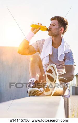 Stock Photograph - Portrait of young attractive man sitting while drinking energy drink. Fotosearch