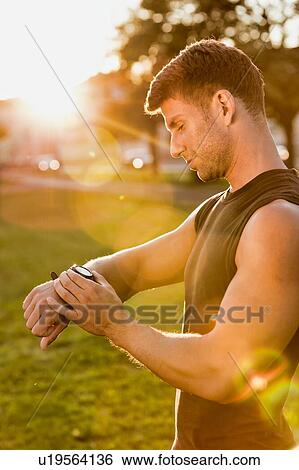 Stock Photograph - Portrait of young attractive man looking at his wristwatch in park with lens flare. Fotosearch
