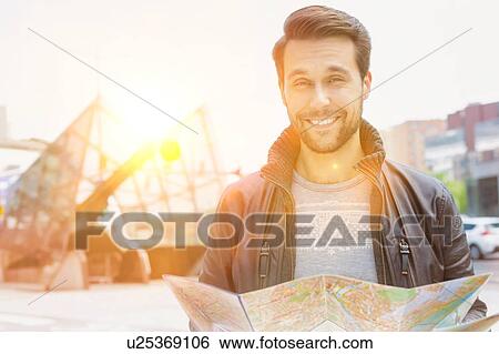 Stock Photograph - Portrait of young attractive man looking on the map in the city with lens flare in background. Fotosearch
