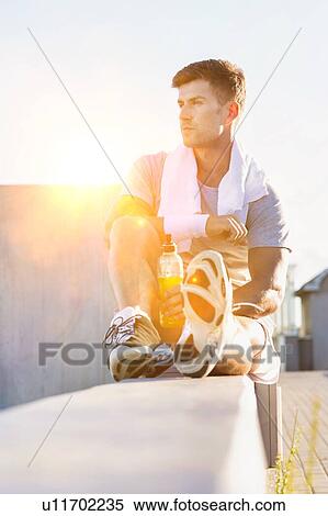 Stock Photography - Portrait of young attractive man sitting while drinking energy drink. Fotosearch