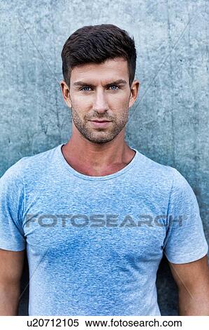Stock Photography - Portrait of young attractive man standing against wall. Fotosearch