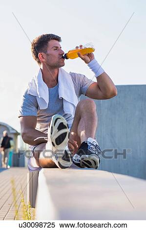 Stock Photography - Portrait of young attractive man sitting while drinking energy drink. Fotosearch